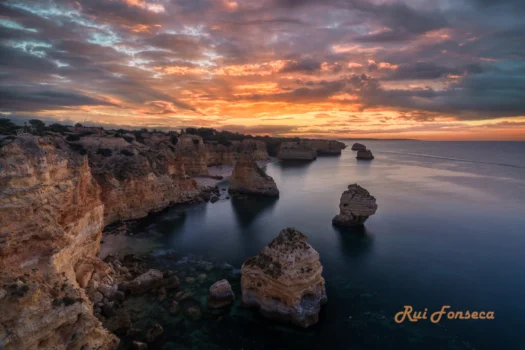 Dramatic sunset over the coastline of Algarve, Portugal, showcasing the iconic rock formations of Ponta da Piedade.