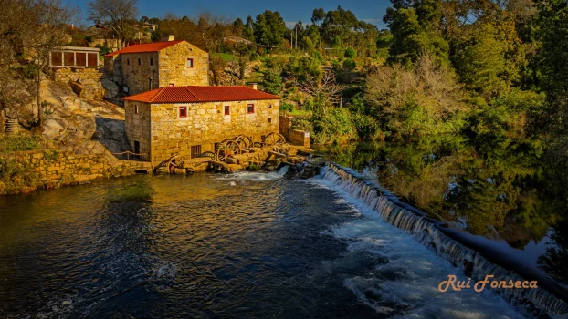 A picturesque view of a historic water mill nestled beside a river, bathed in warm sunlight.