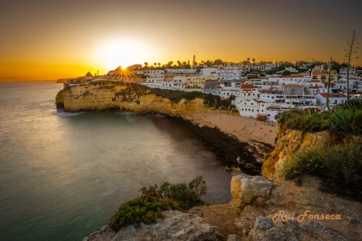 Panoramic view of a coastal town nestled into cliffs, bathed in the warm light of a setting sun.