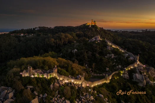 A stunning aerial view of Pena Palace and its surrounding walls at dusk, showcasing the unique architecture and landscape of Sintra, Portugal.