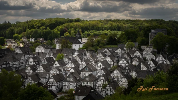 Aerial view of a village with traditional half-timbered houses, lush green trees, and a church steeple in the background.
