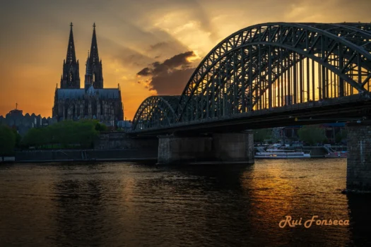 A picturesque view of the Hohenzollern Bridge and the Cologne Cathedral at sunset.