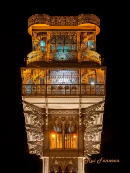 Close-up, nighttime photograph of the intricate, illuminated upper levels of the Torre de Belém in Lisbon, Portugal.