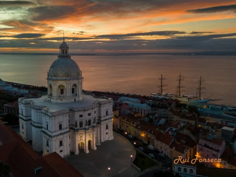 Aerial view of Lisbon, Portugal at sunset, featuring the Basilica da Estrela and a tall ship.