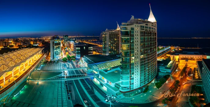 Night view of a modern cityscape with illuminated buildings and a waterfront.