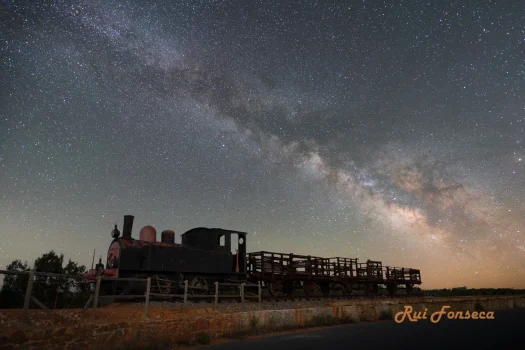 A vintage steam locomotive sits silhouetted against a stunning night sky filled with stars and the Milky Way.