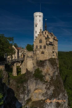 A majestic castle perched atop a rocky outcrop, bathed in sunlight against a clear blue sky.