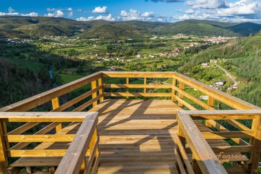 A panoramic view of a valley and mountains from a wooden viewing platform.