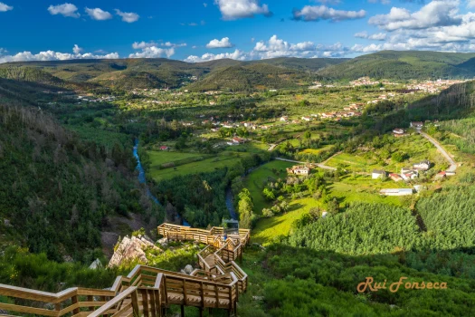 Panoramic view of a valley with a town nestled within rolling hills, viewed from a wooden walkway.