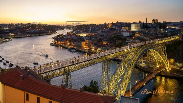 A panoramic view of Porto, Portugal at dusk, featuring the Dom Luís I Bridge illuminated against a vibrant sunset.