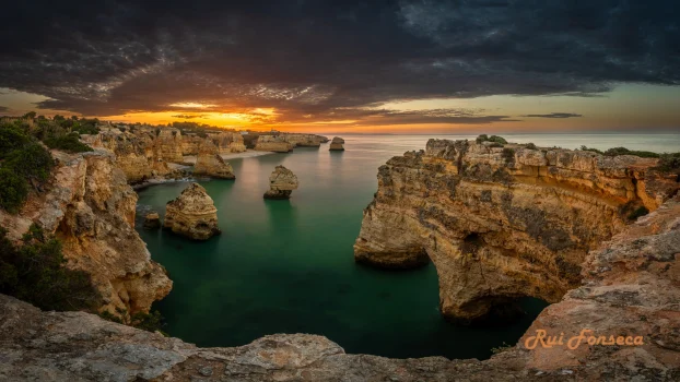 Dramatic sunset over the Algarve coastline, Portugal, showcasing stunning rock formations and turquoise waters.