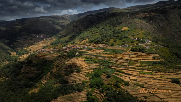 Aerial view of terraced fields and a village nestled in a valley, under a dramatic, cloudy sky.