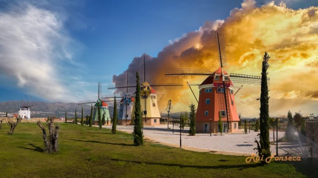 A picturesque landscape featuring a row of colorful windmills against a vibrant sunset sky, captured with a drone.